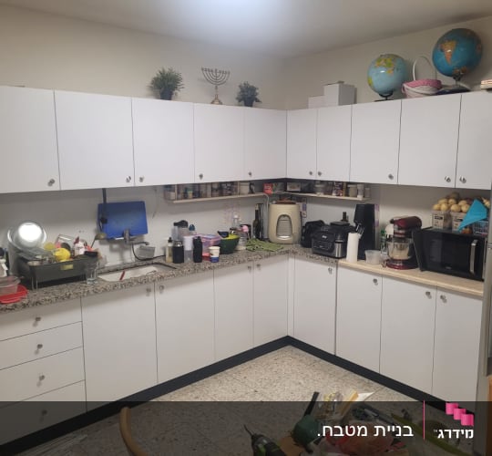 מטבח עם ארונות לבנים וכלי מטבח שונים על השיש